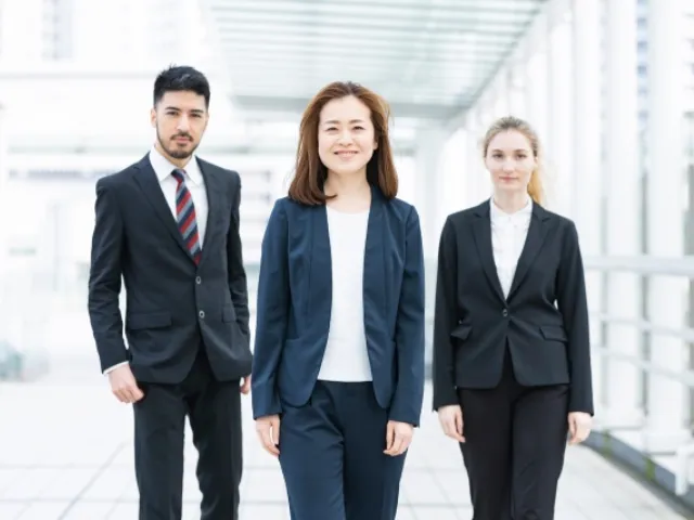 スーツを着た海外の男女二人とその間に立つ笑顔の日本人ビジネスウーマンの画像