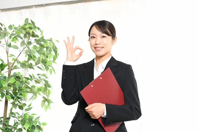 笑顔でOKマークをするスーツ姿の日本人女性の画像