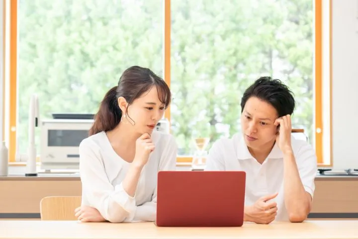 パソコン画面を見ながら悩んでいる夫婦のイメージ