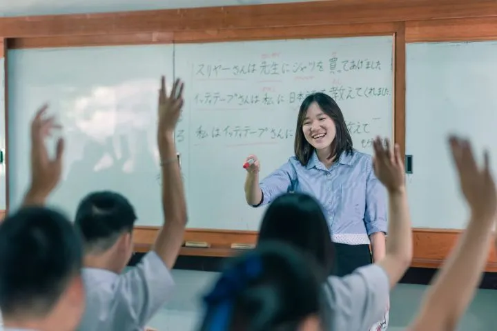日本語教師が手を上げている生徒を選んでいるイメージ