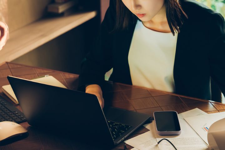 忙しそうにデスクでPCに向かうビジネスウーマンの画像