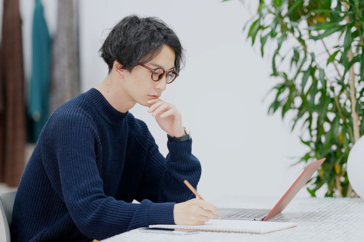 PCで調べものをして、ノートに書いている男性の画像