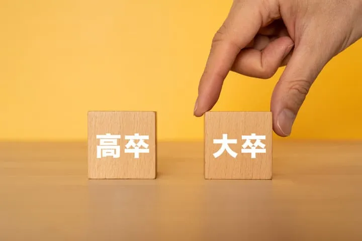 高卒大卒と書かれたブロックを並べ大卒を選ぶ手の画像