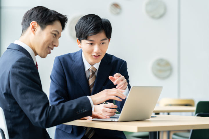 ノートパソコンを見ながら打ち合わせをする日本人ビジネスマン2人の画像
