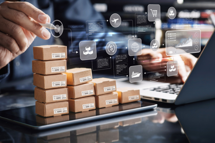 積み上げられたミニチュアの段ボールとパソコンを前に作業する人の画像