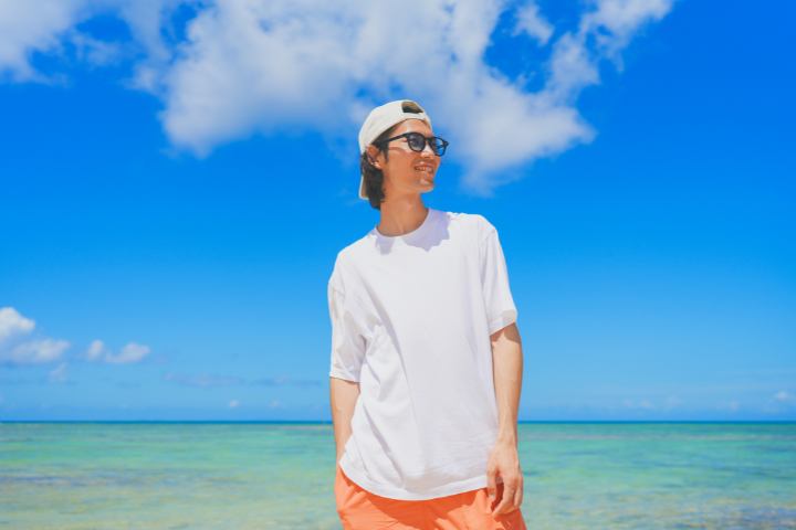 青い海を背に白いTシャツとサングラスの男性の画像