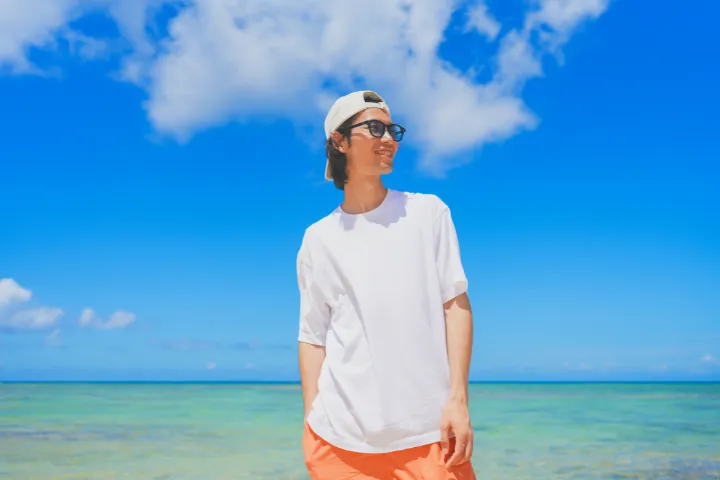 青い海を背に白いTシャツとサングラスの男性の画像