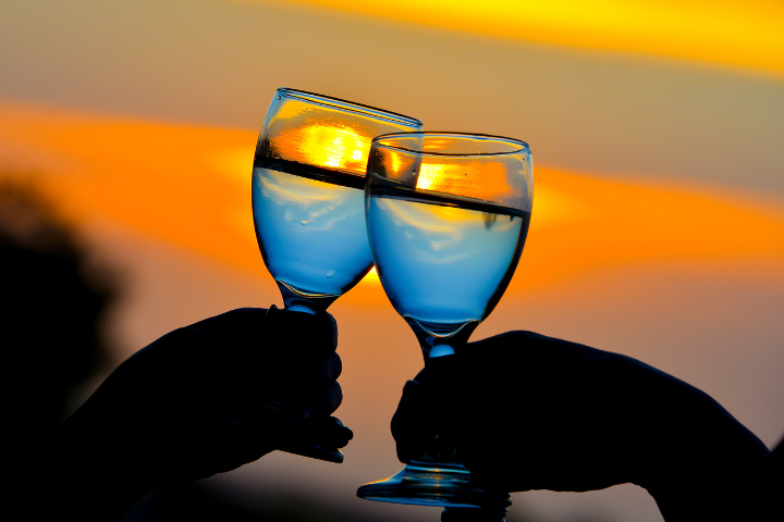 夕日を背景にグラスで乾杯している画像