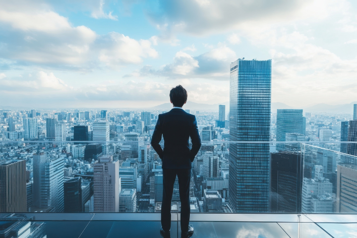 高層階から東京のビル群をみおろす男性会社員の後ろ姿