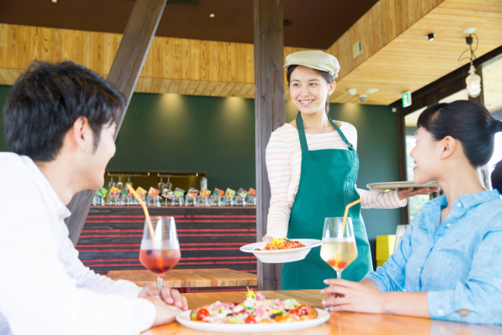カフェで働く日本人女性と笑顔の男女の客の画像