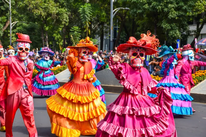 メキシコの死者の日を祝うガイコツの被りものをし色とりどりの衣装に身を包んだダンサー達の画像