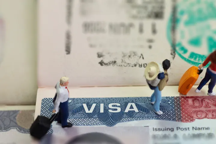 VISAの上にサラリーマンや旅行客のミニチュアが置かれた画像