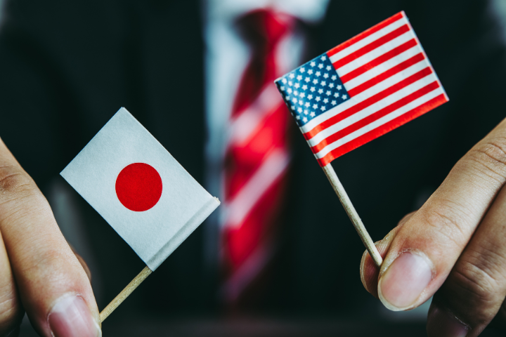 ビジネスマンがミニチュアのアメリカ国旗と日本国旗を持っている画像
