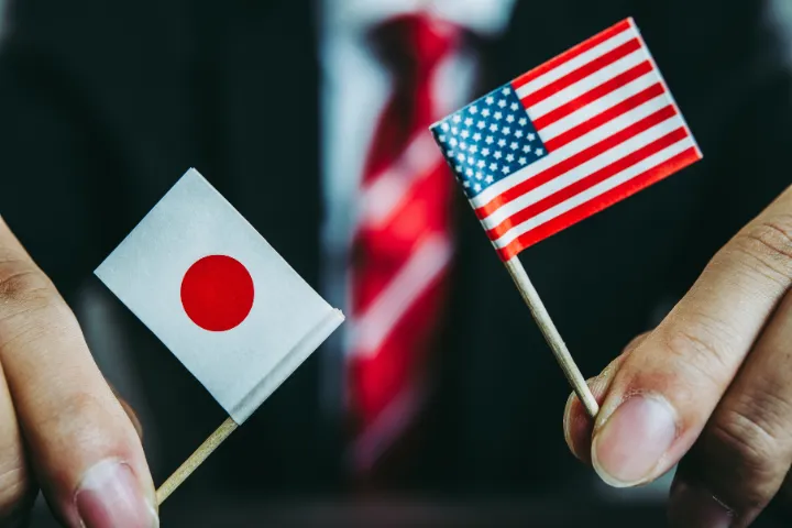 ビジネスマンがミニチュアのアメリカ国旗と日本国旗を持っている画像
