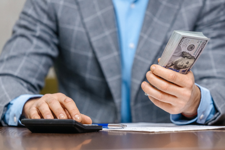 アメリカ紙幣を持ちながら電卓を触るスーツの男性のイメージ