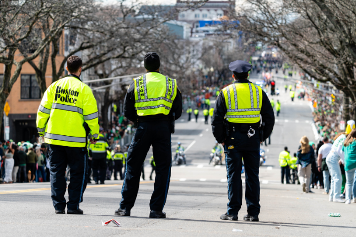 ボストン市警察の警官3人が蛍光色の安全ベストを着用し、通りを練り歩くセント・パトリック・デーのパレードを見守っている