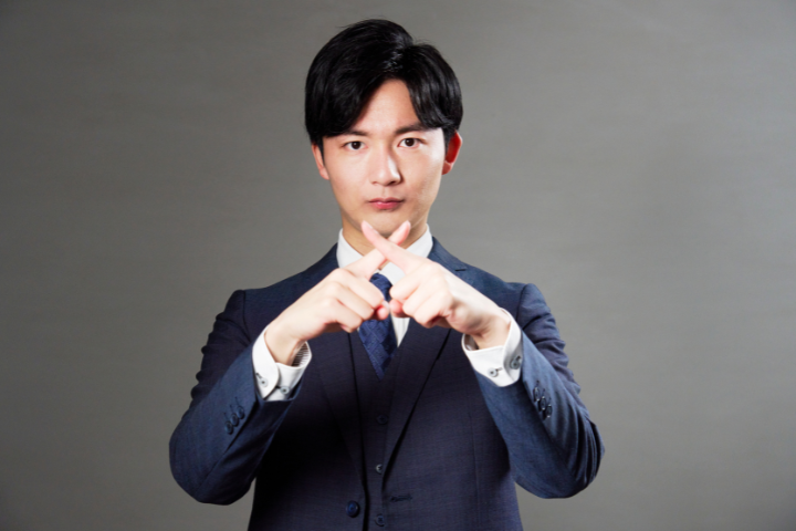 指で罰を作る男性の画像