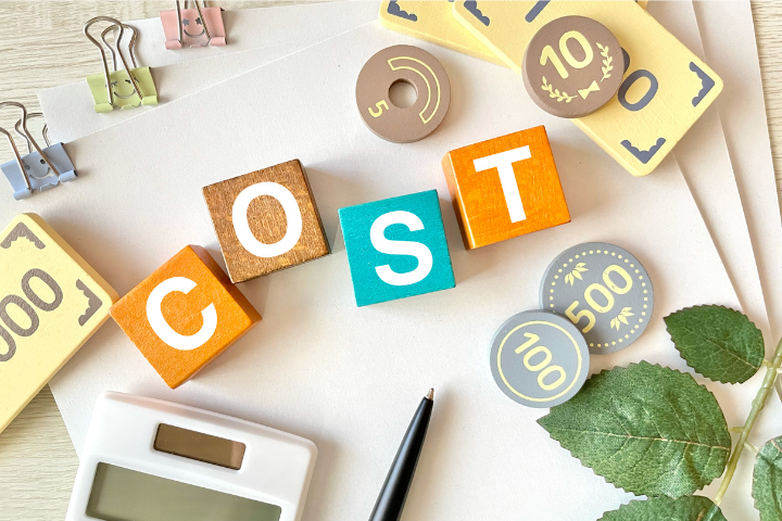 COSTと書かれたブロックとおもちゃのお金と電卓の画像