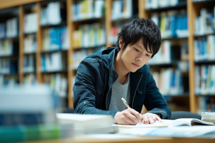 図書館の学習スペースで資格試験の合格に向けて勉強に励む男性の画像